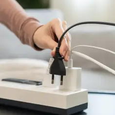 Dłoń podłącza wtyczkę do listwy zasilającej, symbolizując zarządzanie energią w nowoczesnym domu, który jest kluczowy dla rozwoju smart grid.