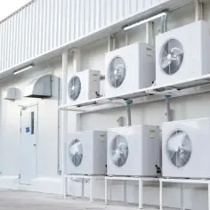 Rząd białych jednostek klimatyzacyjnych zamontowanych na ścianie budynku.