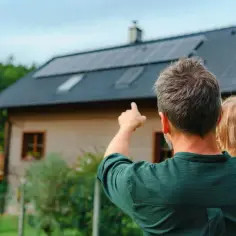 Ojciec z córką patrzą na dom z panelami fotowoltaicznymi. Ciekawi ich instalacja fotowoltaiczna 6 kw cena.