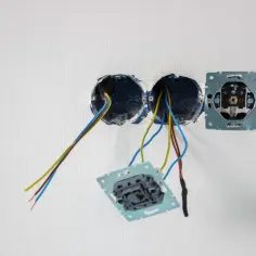 Osadzanie puszek elektrycznych: widoczne przewody wychodzące z dwóch okrągłych puszek, obok zamontowana ramka gniazdka.