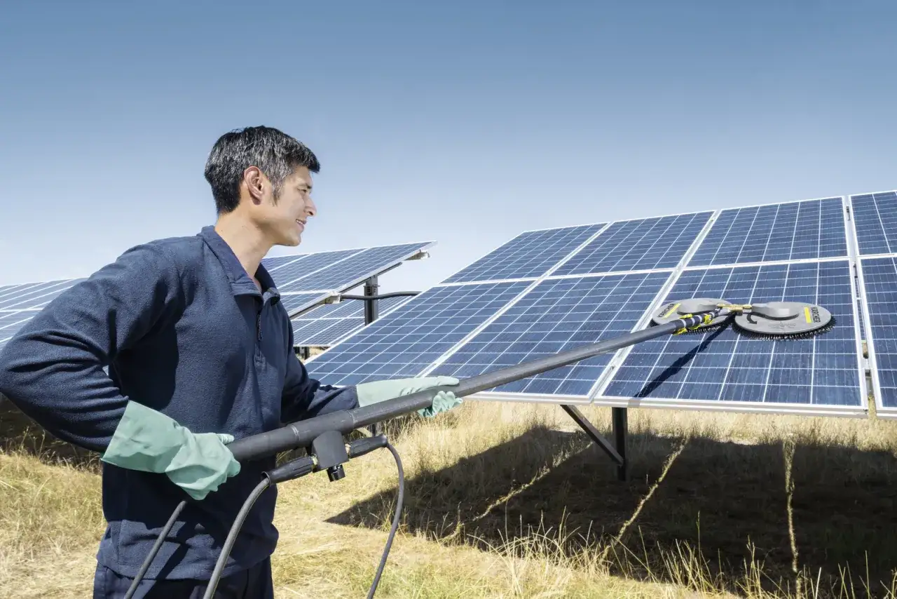 Mężczyzna w rękawiczkach czyści panele fotowoltaiczne specjalną szczotką. Czyste panele to lepsza produkcja energii.