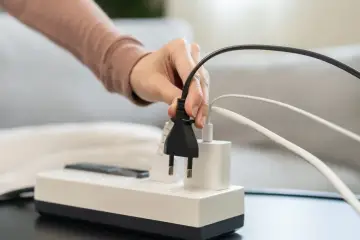 Dłoń podłącza wtyczkę do listwy zasilającej, symbolizując zarządzanie energią w nowoczesnym domu, który jest kluczowy dla rozwoju smart grid.